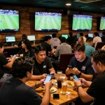 Kèo nhà cái sports betting scene with live match displays and excited patrons using mobile apps